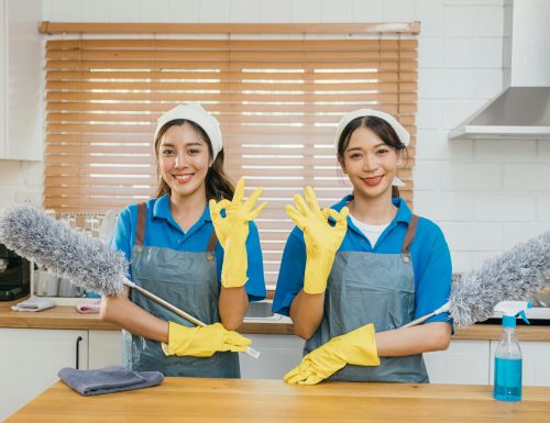 Cleaning service women in uniform stand on kitchen counter holding duster foggy spray and rag