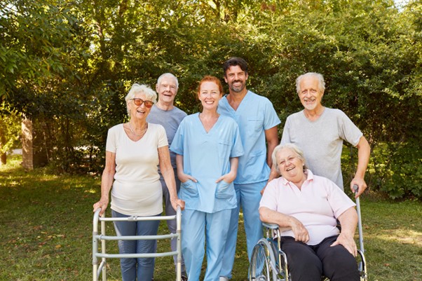 A group of smiling seniors and caregivers pose together outdoors, showcasing the compassion and teamwork caregivers bring to in-home senior care.