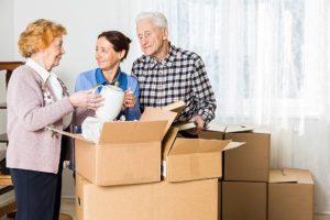 Two seniors and a caregiver unpack moving boxes together, highlighting how reducing clutter and organizing the home can positively impact senior mental health.