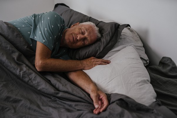 An elderly man sleeping in bed during the day, highlighting common challenges related to sleep disorders in aging adults.