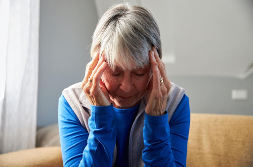 An elderly woman sits with her head in her hands, appearing overwhelmed, symbolizing how regular companionship and caregiver visits can ease anxiety and provide emotional relief.