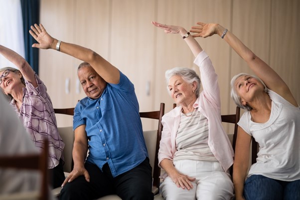 A group of seniors participates in a seated stretching exercise, demonstrating how light daily movement like chair Zumba supports balance and reduces fall risk.