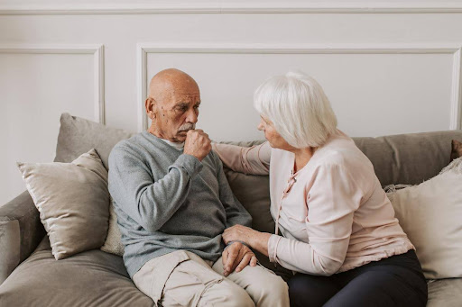 An elderly man struggles with his breathing while sitting on a couch, comforted by a woman beside him—illustrating how home care support can ease daily challenges for those living with COPD.