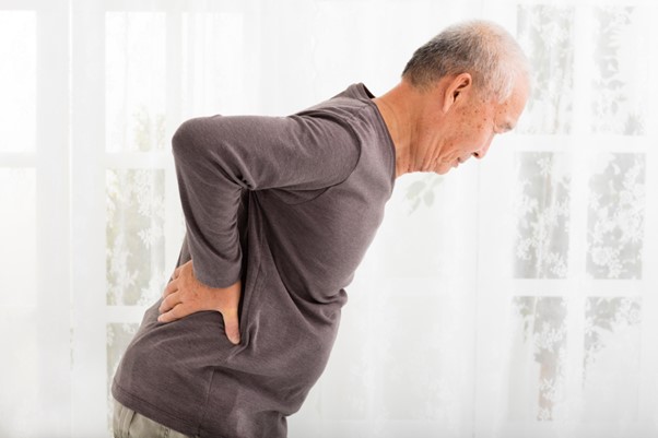 An elderly man holds his lower back in pain, illustrating the daily challenges of arthritis and the importance of home modifications and home care support for relief and mobility.