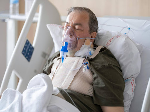 An elderly man rests in a hospital bed wearing an oxygen mask, illustrating the critical recovery phase where concierge services can provide personalized support and ease the healing process at home.