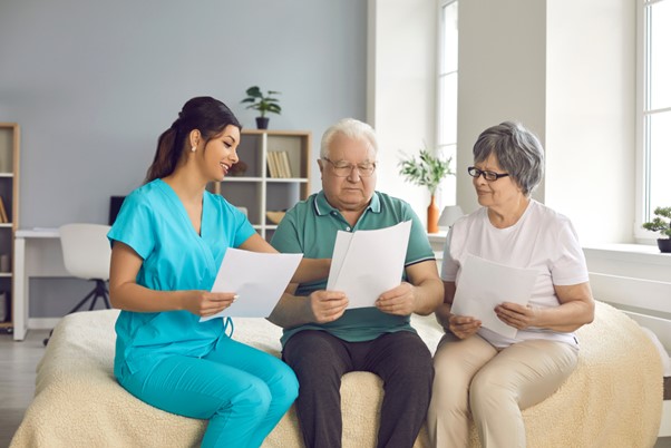 A caregiver discusses documents with two older adults, symbolizing the emotional and logistical challenges—like sibling guilt—that can arise when arranging home care for aging parents.