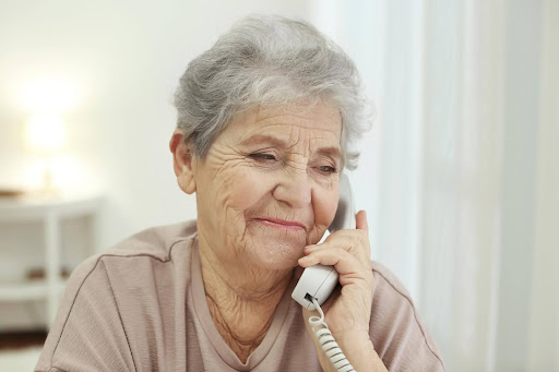 An elderly woman smiles gently while talking on the phone, reflecting the comfort and emotional connection a friendly voice can bring to combat senior loneliness.