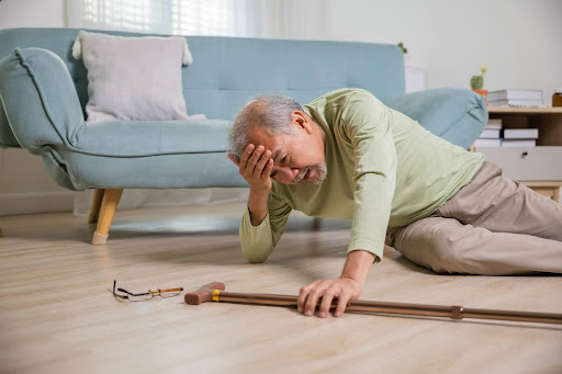 An elderly man lies on the floor reaching for his cane, looking distressed—emphasizing the serious risks and warning signs that even a single fall can represent for senior health and safety.