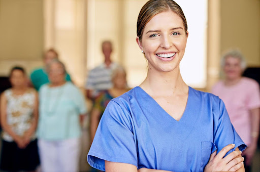 A confident young caregiver smiles in the foreground with a group of seniors blurred behind her, embodying the qualities of a great caregiver—compassion, presence, and dedication beyond formal training.