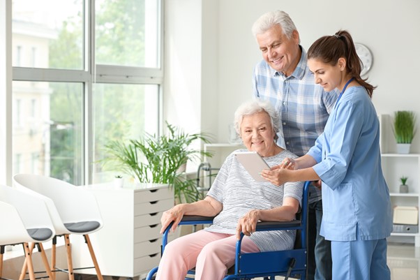 A caregiver shows a digital tablet to an elderly woman in a wheelchair while her companion looks on, illustrating the guidance and planning involved in choosing the right senior home care services.