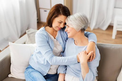 A middle-aged woman lovingly embraces her elderly mother on a couch, reflecting a caring decision-making moment about whether home care is the right choice for their aging parent.