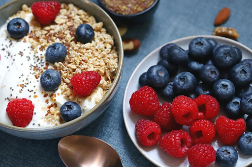 A colorful and appetizing bowl of yogurt topped with granola, blueberries, and raspberries, served alongside a plate of fresh berries—demonstrating how vibrant colors and textures can help stimulate appetite in seniors.