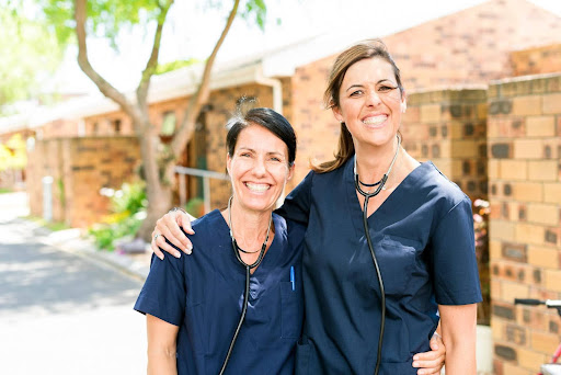 Two smiling female caregivers in navy scrubs stand outdoors with their arms around each other, symbolizing the different types of caregivers available to support various client needs.