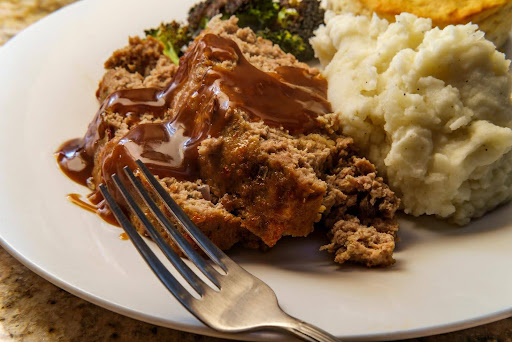 A hearty meal cooked for seniors, featuring meatloaf with gravy, mashed potatoes, and vegetables—evoking familiar flavors from the 1940s.