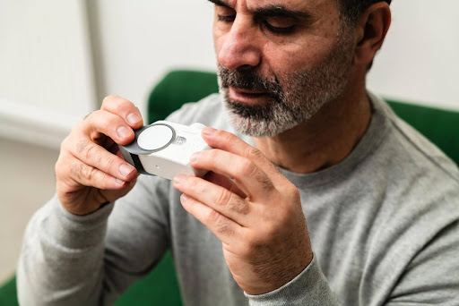 A middle-aged man closely examines a medical inhaler, highlighting the importance of allergen-free environments and specialized cleaning for clients with COPD, asthma, and other respiratory issues.