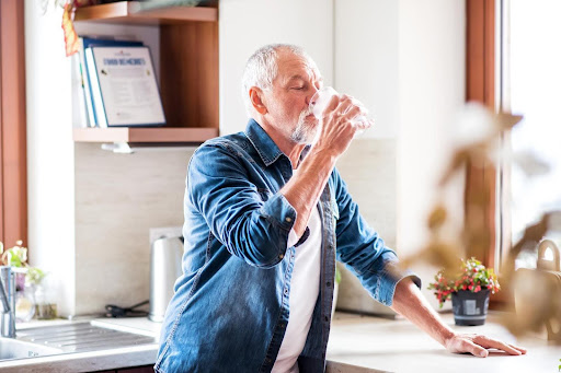 Senior man drinking a glass of water in a modern kitchen, emphasizing the importance of hydration for elderly health and memory support.