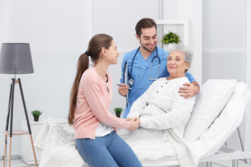A smiling elderly patient sits in a hospital bed, supported by a nurse and a family member, representing the compassionate care that many patients receive through home health services.