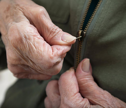 Close-up of an elderly woman's hands struggling to zip her dress, representing the need for compassionate daily assistance.