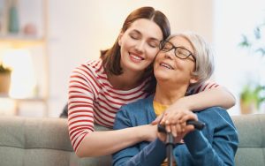 A joyful adult daughter warmly hugs her elderly mother, both smiling with eyes closed—capturing the emotional bond and challenges families face when navigating senior care decisions.