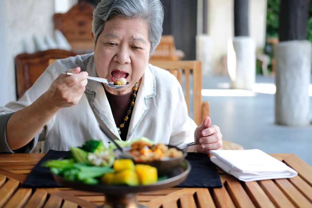 Elderly woman eating a healthy meal at a wooden table, highlighting solutions for seniors who often skip meals due to non-hunger-related reasons.