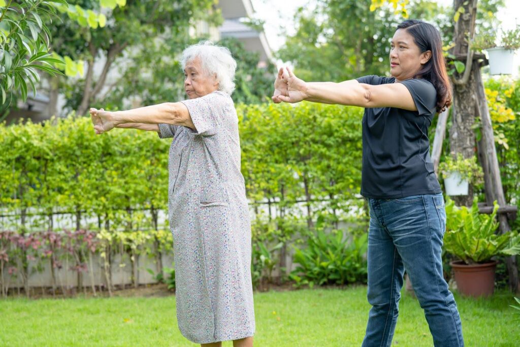 Senior woman doing outdoor stretches with a caregiver, symbolizing simple home modifications and support for seniors with arthritis.