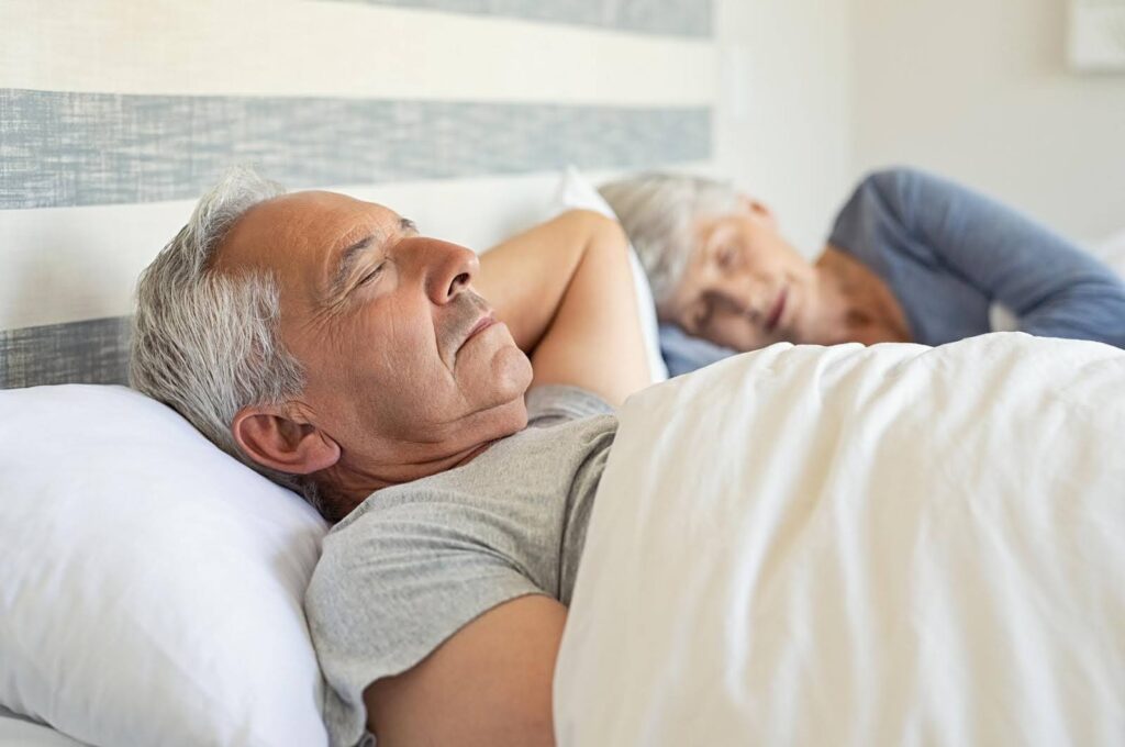 Elderly couple peacefully sleeping in bed, highlighting the importance of proper sleep habits for senior health and how caregivers can support restful sleep.
