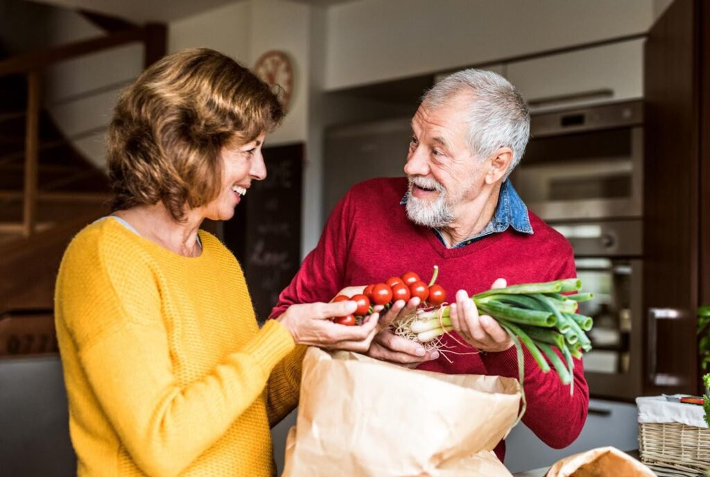 Smiling elderly couple unpacking groceries together in their kitchen, representing how concierge care services provide flexible, personalized support compared to full-time aides.