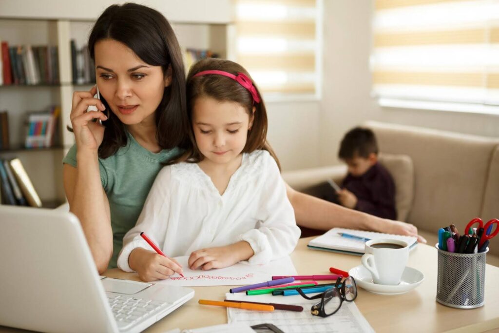 Busy mother working from home while caring for children, representing the need for senior concierge services to support long-distance families.