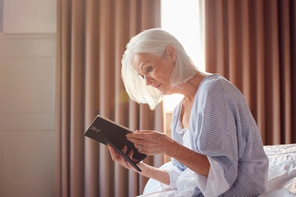 Elderly woman sitting on a bed and looking thoughtfully at a framed photo, symbolizing grief and how companion care can provide comfort and support after the loss of a spouse.