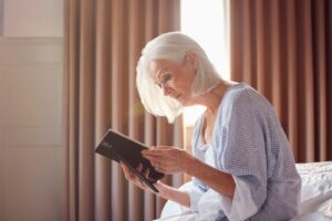 Elderly woman sitting on a bed and looking thoughtfully at a framed photo, symbolizing grief and how companion care can provide comfort and support after the loss of a spouse.