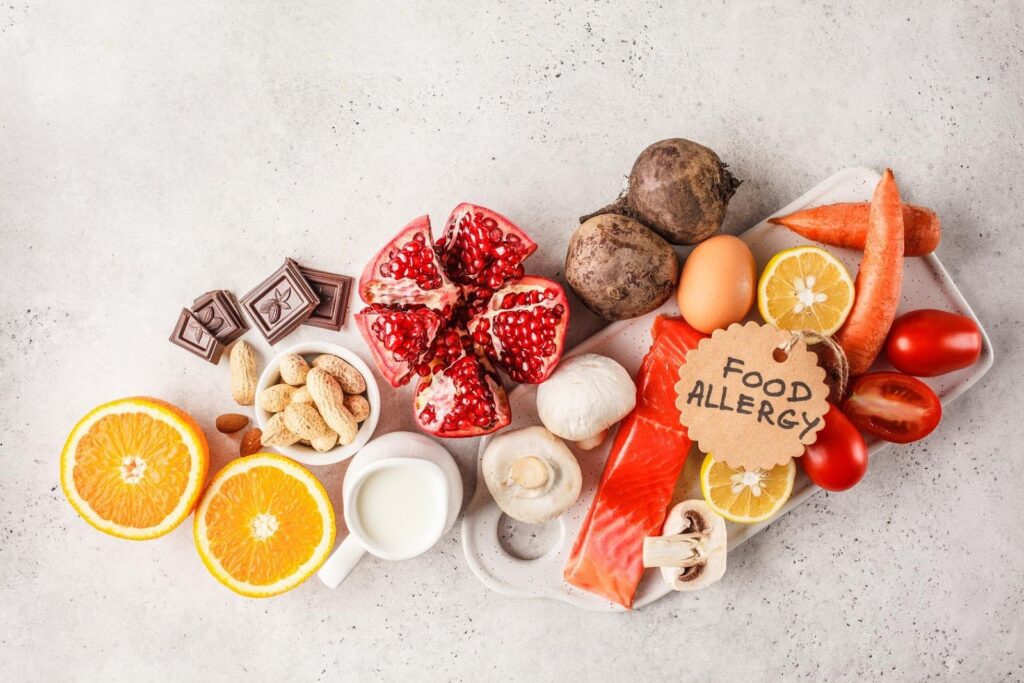 Assorted foods like nuts, milk, fish, eggs, and citrus arranged with a tag labeled 'Food Allergy,' highlighting safe meal prep for seniors with allergies.