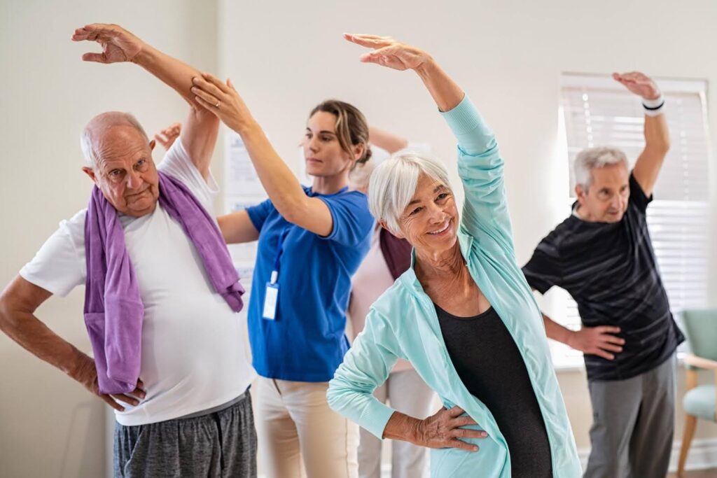 Group of smiling seniors participating in a guided stretching class, showing how regular group fitness activities like Zumba can improve health and reduce hospital visits.
