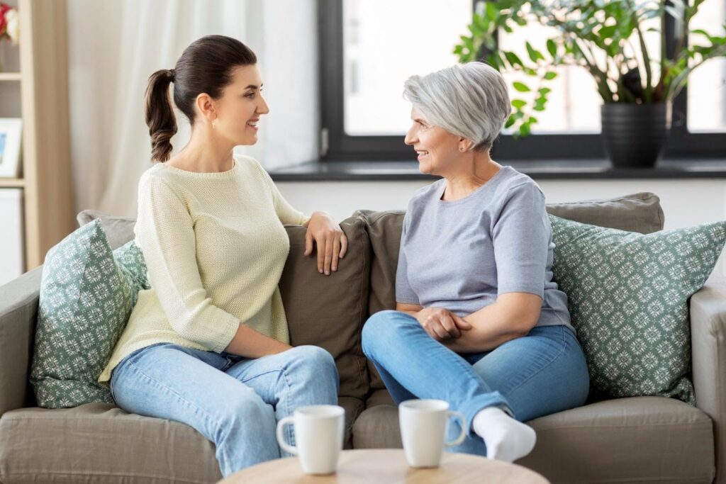Caregiver and senior woman sitting on a couch having a warm conversation, showing how visits can be meaningful and supportive.