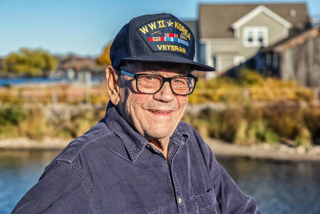 Smiling veteran wearing a service cap outdoors, representing the need for emotional support and specialized care for veterans and retired professionals.