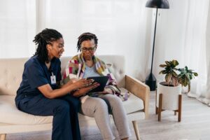 Caregiver showing a tablet to a senior woman on a couch, representing the importance of culturally matched caregivers for senior well-being.