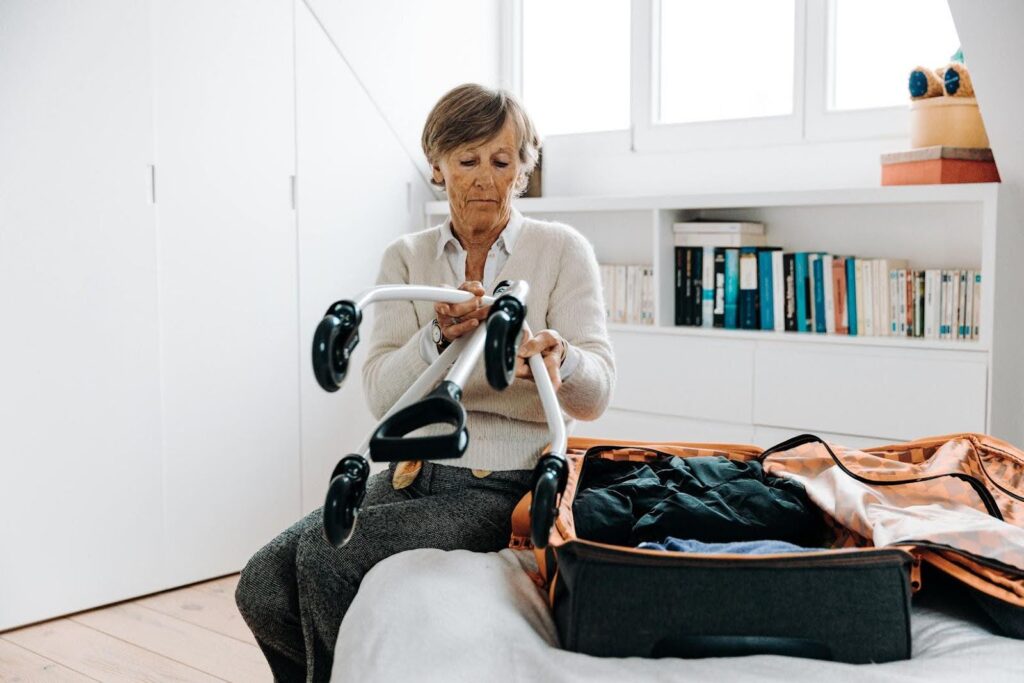 Elderly woman sitting on her bed packing a suitcase and preparing a mobility aid, representing a calm and empowering morning routine that helps seniors maintain independence and confidence.