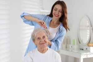 Smiling caregiver gently combing an elderly woman’s hair, representing compassionate support with personal hygiene needs.