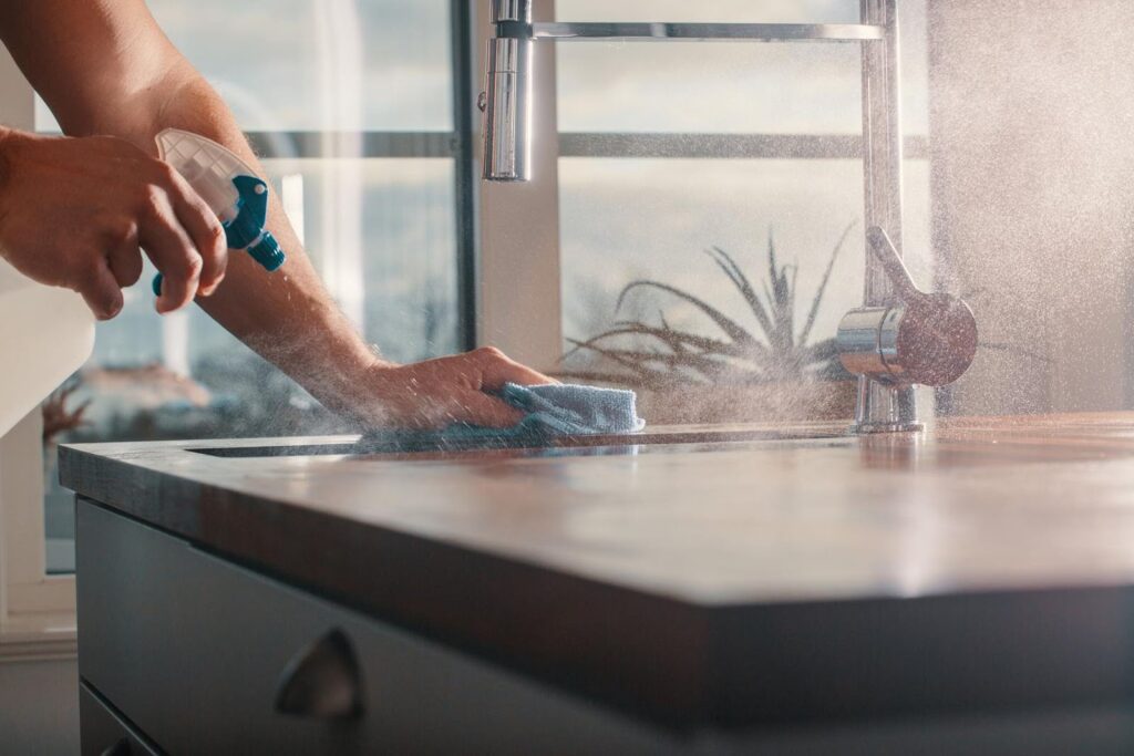 Person cleaning a kitchen counter, representing the importance of clean and organized spaces for seniors living alone.