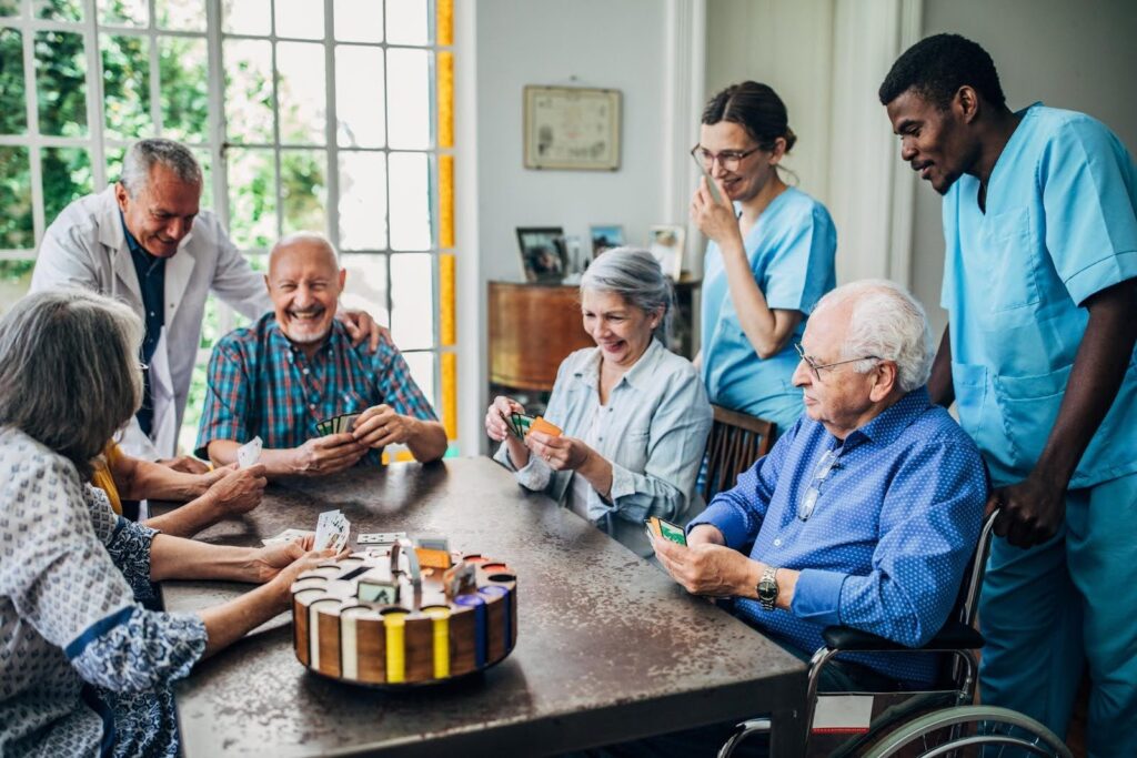 Group of seniors enjoying activities with caregivers in a supportive home setting, illustrating how home care can delay nursing home admission.