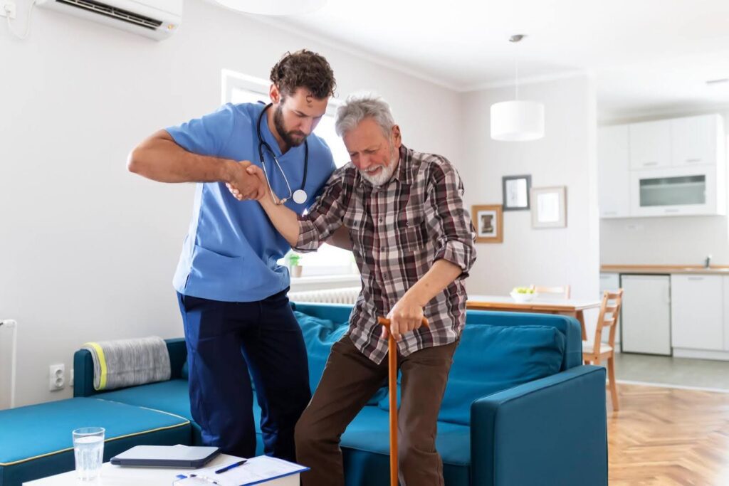 Caregiver helping an elderly man stand up at home, showing early signs that a loved one may need more than light help around the house.