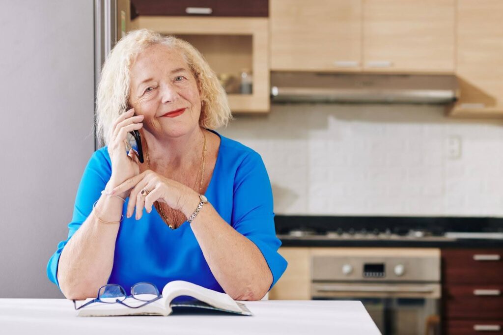 Smiling senior woman talking on the phone at home, showing how reassurance calls can bring comfort and connection without feeling clinical.