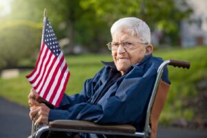 Retired veteran in a wheelchair holding an American flag, representing how Ace Home Care provides compassionate, specialized home care for retired veterans.