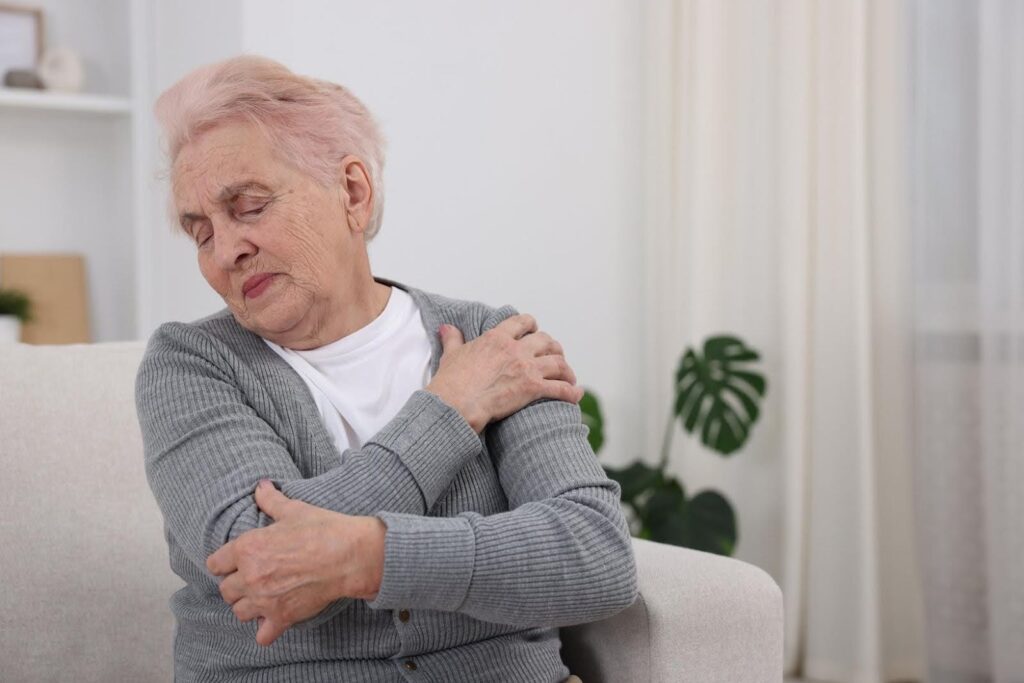 Senior woman experiencing shoulder pain and limited arm mobility at home, highlighting daily support and care assistance provided by Ace Home Care.