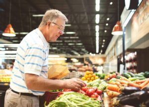 Elderly man grocery shopping for fresh produce with assistance from Ace Home Care services.