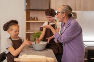 Grandchildren baking with their aging grandmother at home, highlighting Ace Home Care's support in helping grandchildren stay connected with aging grandparents through meaningful family moments.