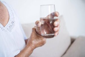 Older adult with essential tremor holding a glass of water, showing everyday challenges that may require supportive home care from Ace Home Care.