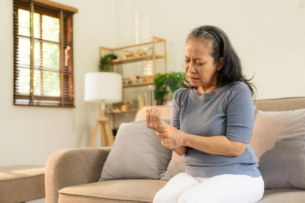 Older adult experiencing hand discomfort from Peripheral Neuropathy at home, highlighting nerve symptoms that may also affect balance and walking.
