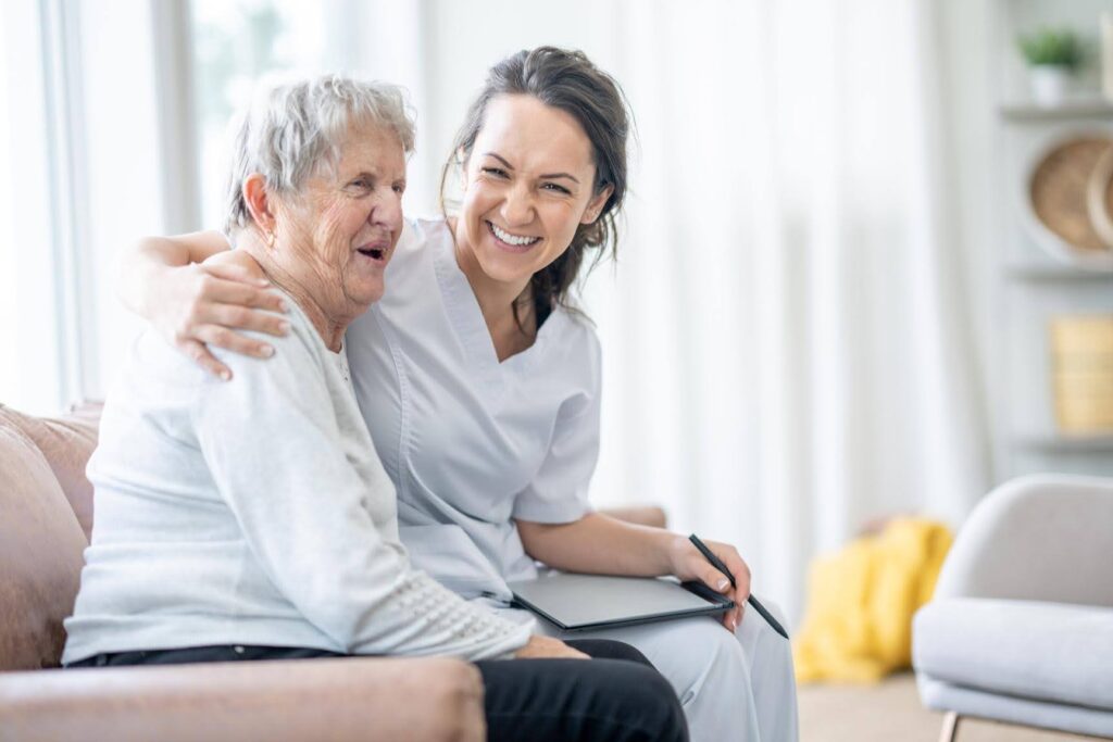 Smiling caregiver sitting beside an elderly woman at home, highlighting how part-time and daily home care provide companionship and personalized support for seniors.