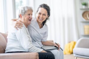Smiling caregiver sitting beside an elderly woman at home, highlighting how part-time and daily home care provide companionship and personalized support for seniors.