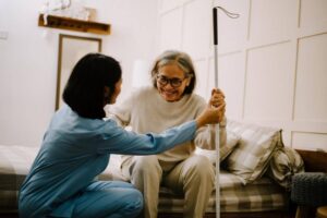 Home care caregiver gently assisting an elderly woman sitting on her bed with a walking cane, helping her feel comfortable and supported during her first in-home care experience.